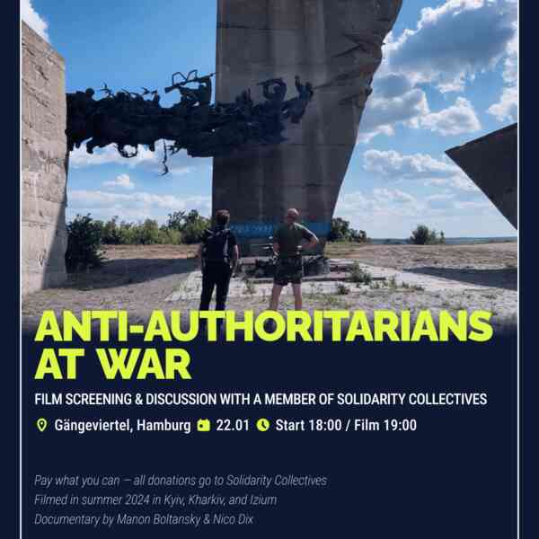 Filmstill: Zwei Personen von hinten — eine in schwarzer Kleidung mit Rucksack, eine in olivgrüner Armeeuniform — stehen vor einem massiven sowjetischen Kriegsdenkmal mit Bronzefiguren kämpfender Soldaten. Am Sockel steht „Слава Україні" (Ruhm der Ukraine). Blauer Himmel mit Wolken, Sommer 2024.